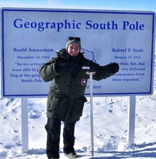 Captain Shelby Kniss standing in full winter gear on snowy ground in front of sign that says "Geographic North Pole".