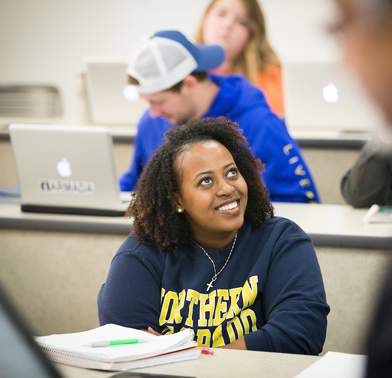 Student in a Northern Colorado sweatshirt smiling attentively in a classroom setting.