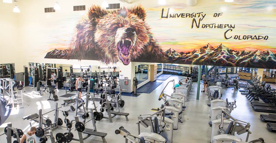 The inside of the Campus Recreation Center, depciting the Bear Mural on the wall as well as the gymnasium equipment in the room.