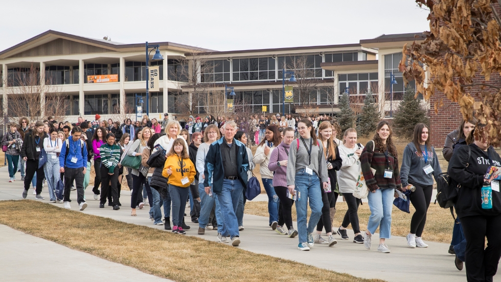 A large group of high school students and their families who attended the Future Teacher Conference are walking outside the University Center building to start their campus tour