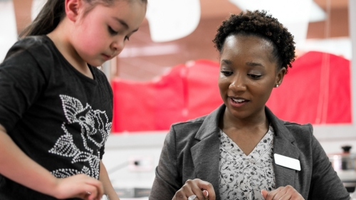 a young female student is working on her crafts with her teacher at the table.