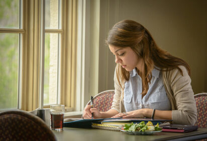 A girl fills out a form whilst sitting at a table in a house.