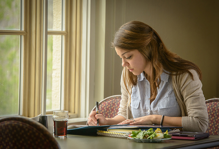 A girl fills out a form whilst sitting at a table in a house.