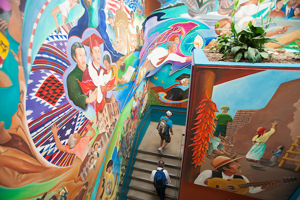 Two students walking up the stairs in Candeleria Hall, the life and times of Dr. Martin mural on the walls