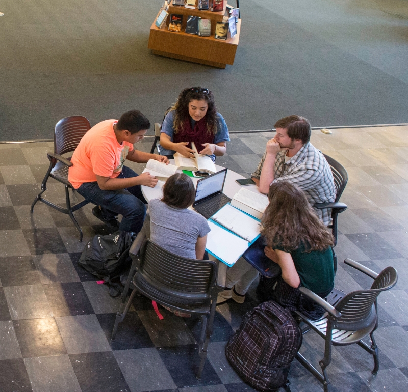 a group of five students are huddled around a circle table working on a project together. This is an aerial view of their collaboration.
