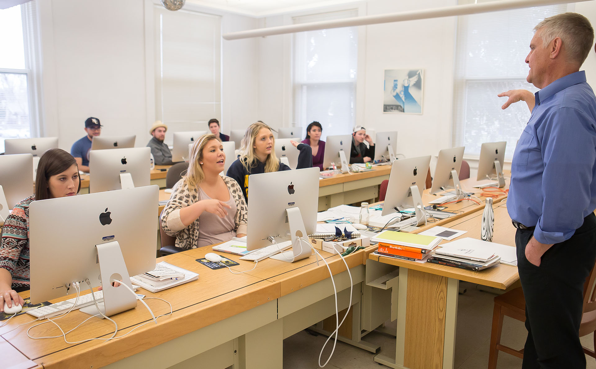 A professor speaks to his students in a computer lab.