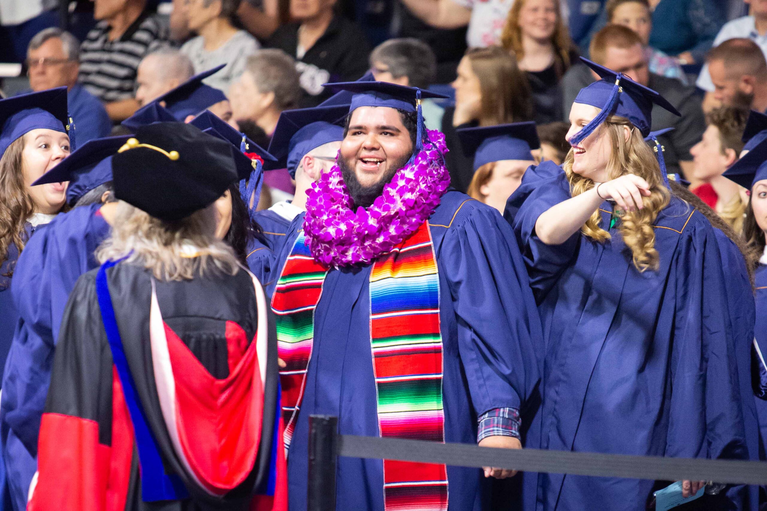 Graduate wearing a flower necklace smiles at commencement.