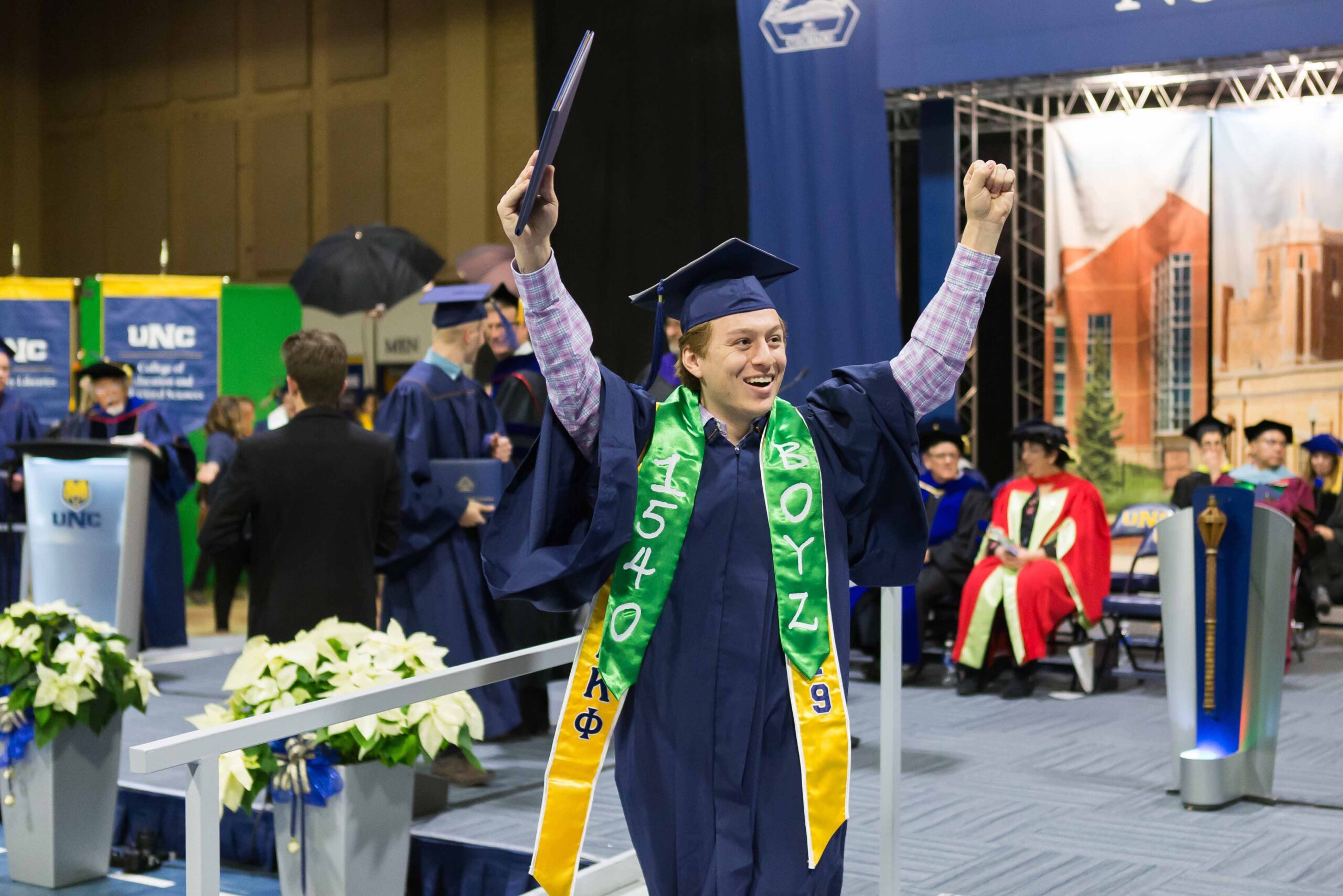 Graduate raise his diploma and fist above his head in celebration at commencement.