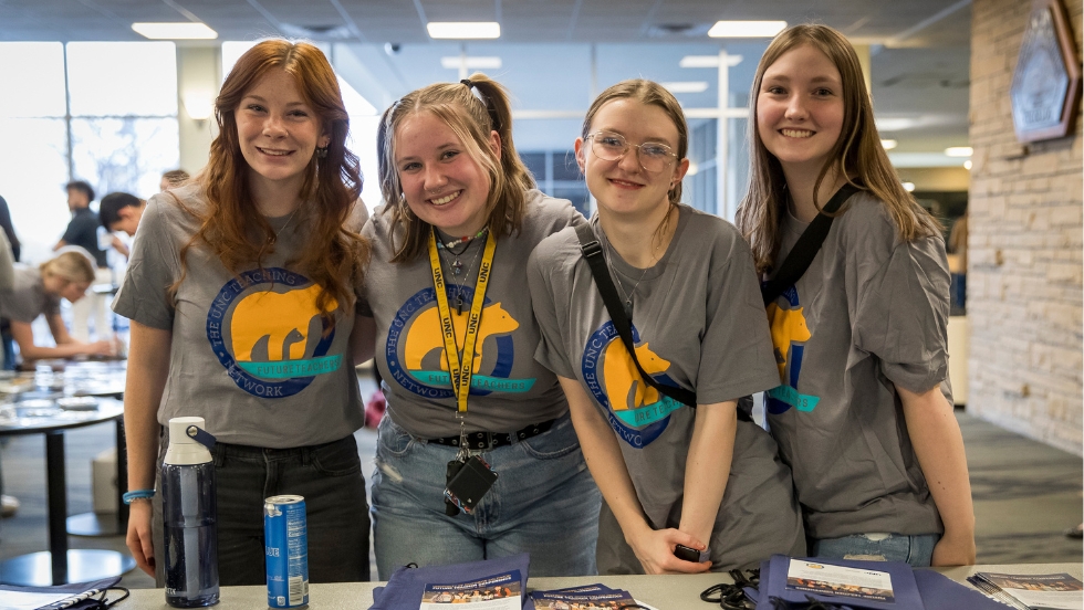 four female student volunteers pose for a picture while handing out brochures and bags for the Future Teacher Conference