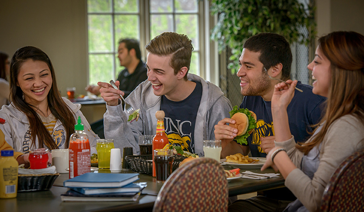 Several students laugh while eating lunch in the dining room.