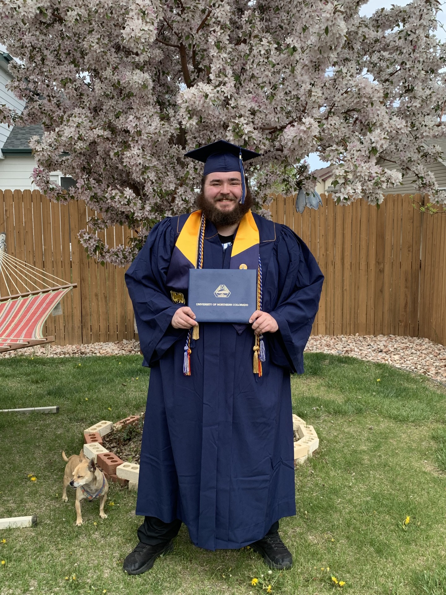 A photo of Alumni Ajax Nelson in his graduation cape and gown with his diploma in his hand