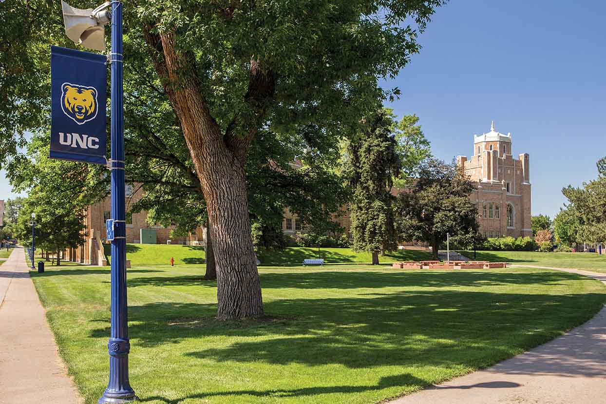 UNC's front campus, Gunter Hall in the background, stonehinge monument just in front of it, followed by a lightpole with a UNC banner on it.