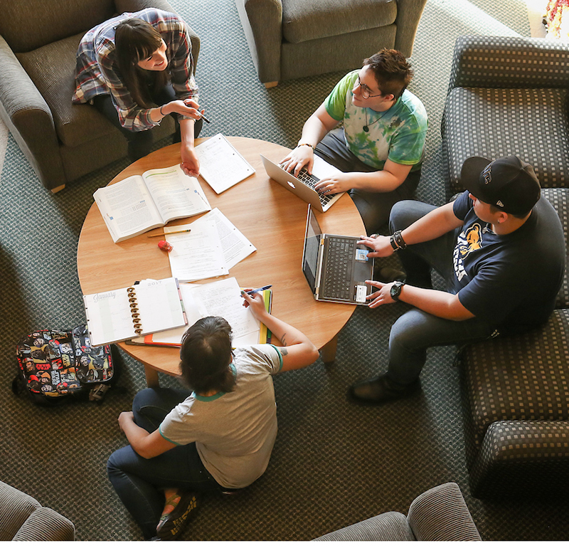 An aerial view of students sitting around a table with laptops and books, engaged in discussion and collaborative learning.