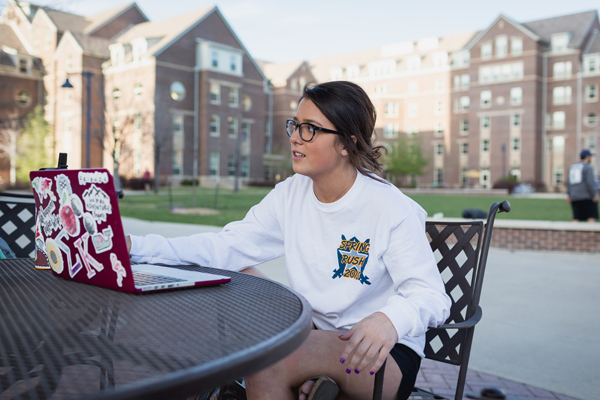 A student wearing glasses studies outside sitting at a table with her laptop.