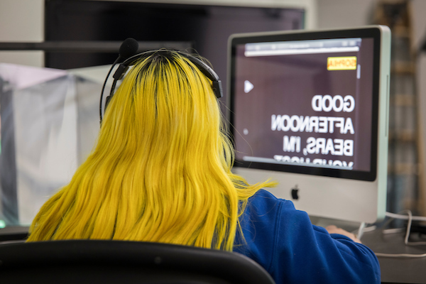 A student with yellow hair working on a Apple Computer during a Journalism class