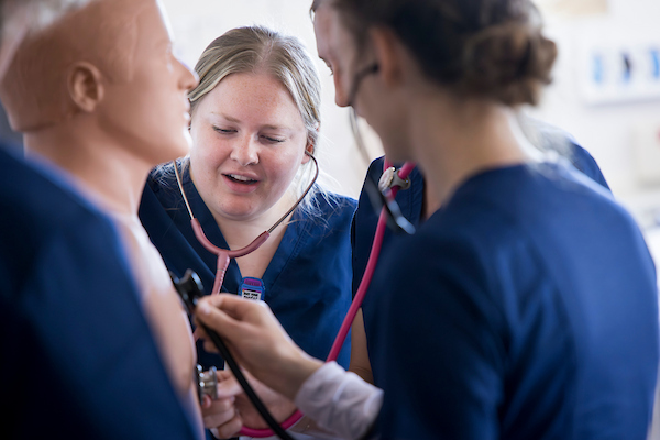 Nursing Students in scubs practicing stethoscope usage