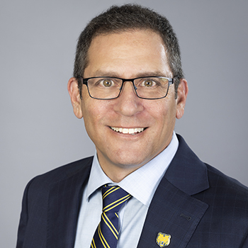 Middle age man, dressed in a blue suit, smiling with a dark grey background
