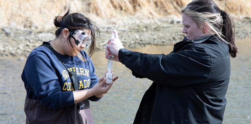 Two students testing the quality of the Cache la Poudre River.