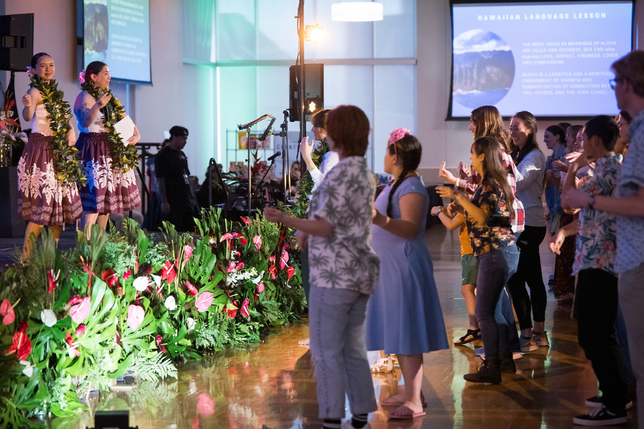Guests dance in a crowd while hispanic women in intricate dresses dance on a stage.