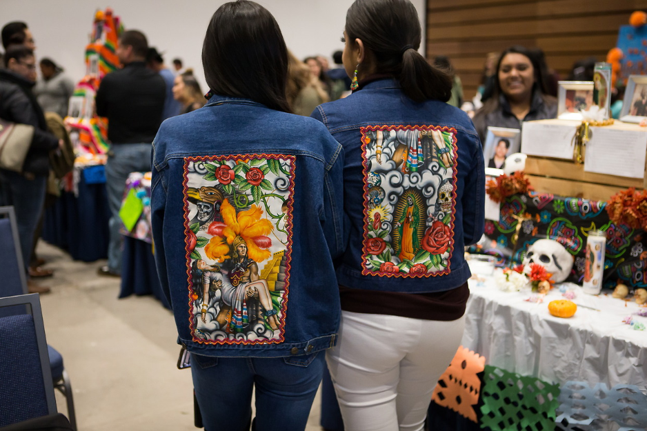 Two students stand together wearing jean jackets with painted backs.