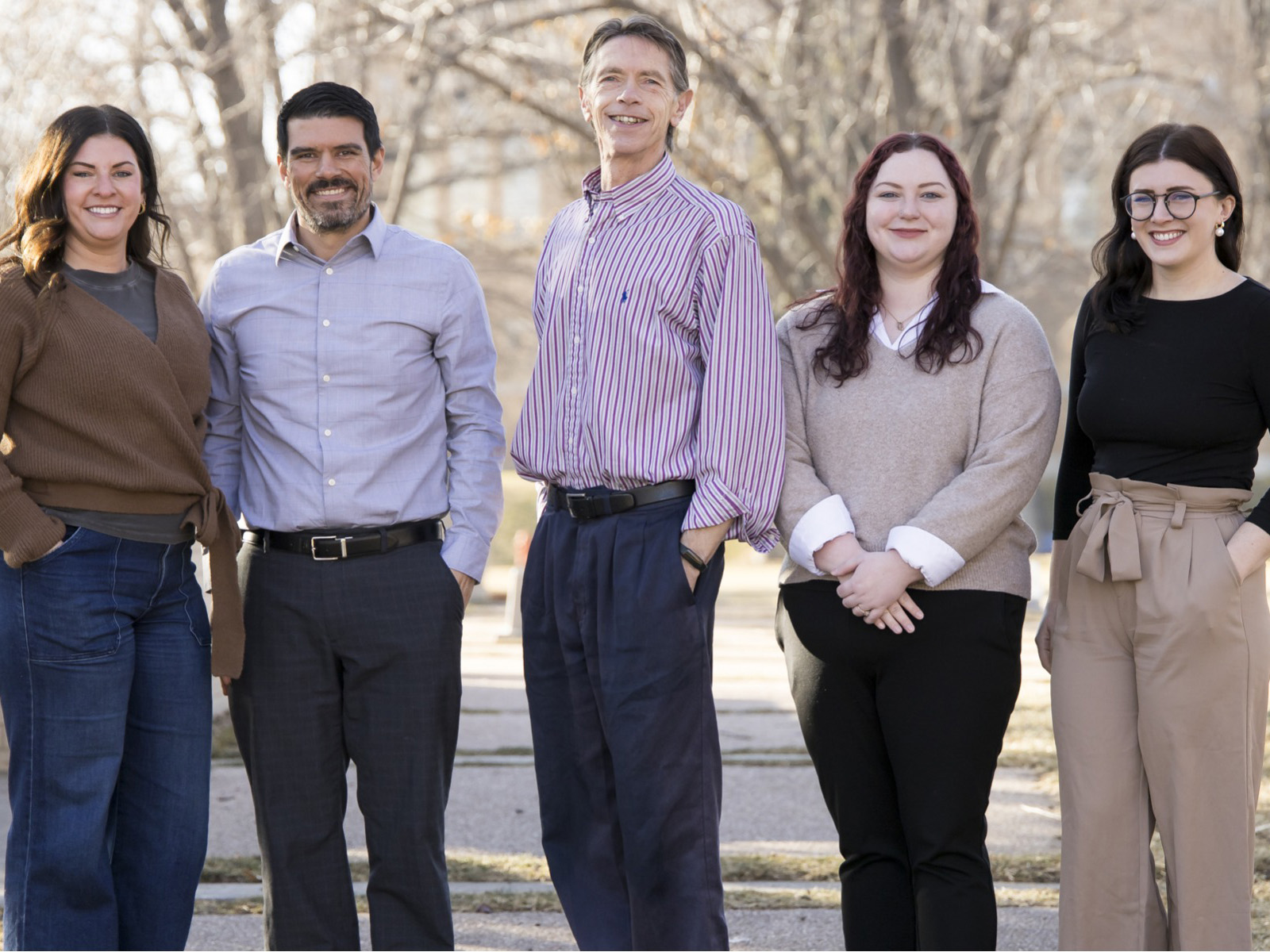 A group of people wearing business attire clothing. Smiling for a photo outside.