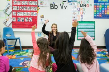 Early Childhood education student working in a classroom with kids raising their hands