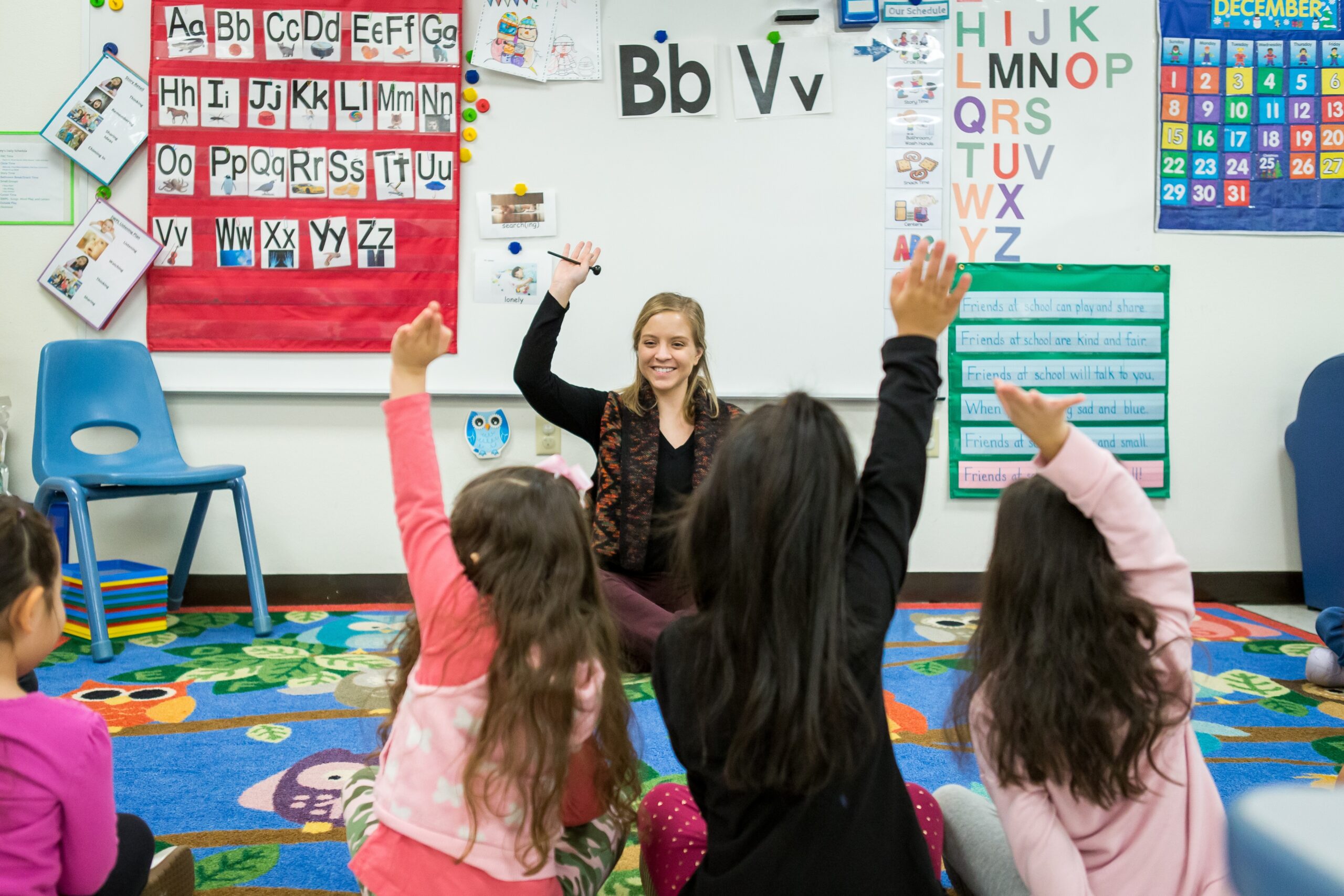 Early Childhood education student working in a classroom with kids raising their hands