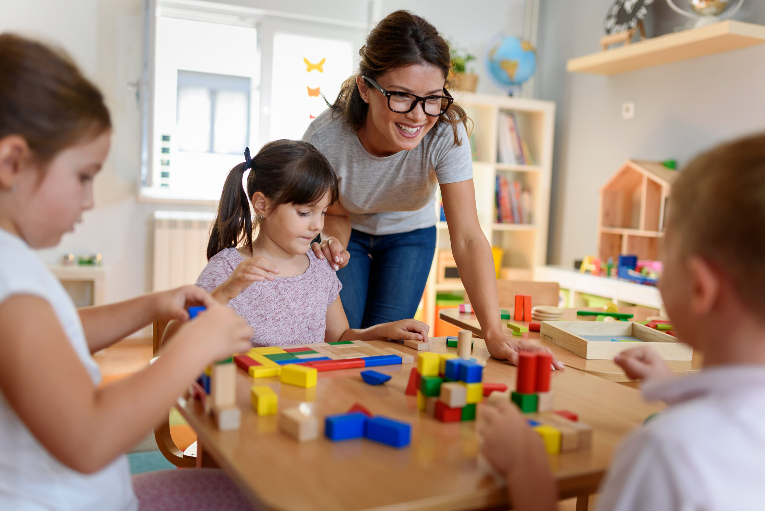 Preschool teacher with children playing with colorful wooden toys
