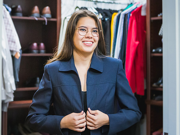 A young woman, dressed in a blue suit jacket smiling. She is surrounded by other articles of clothing