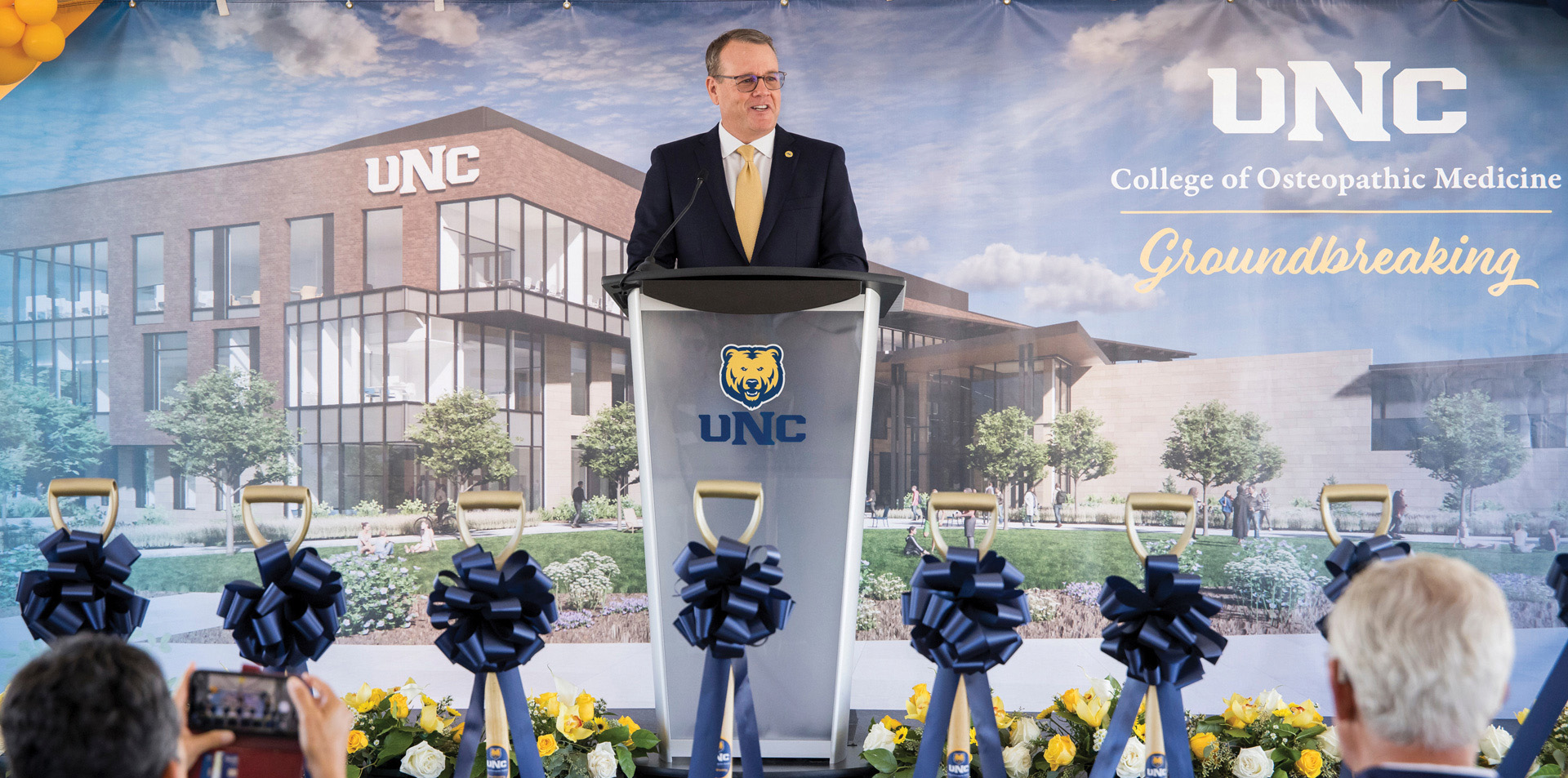 Andy Feinstein standing at a podium with a College of Osteopathic Medicine backdrop behind him