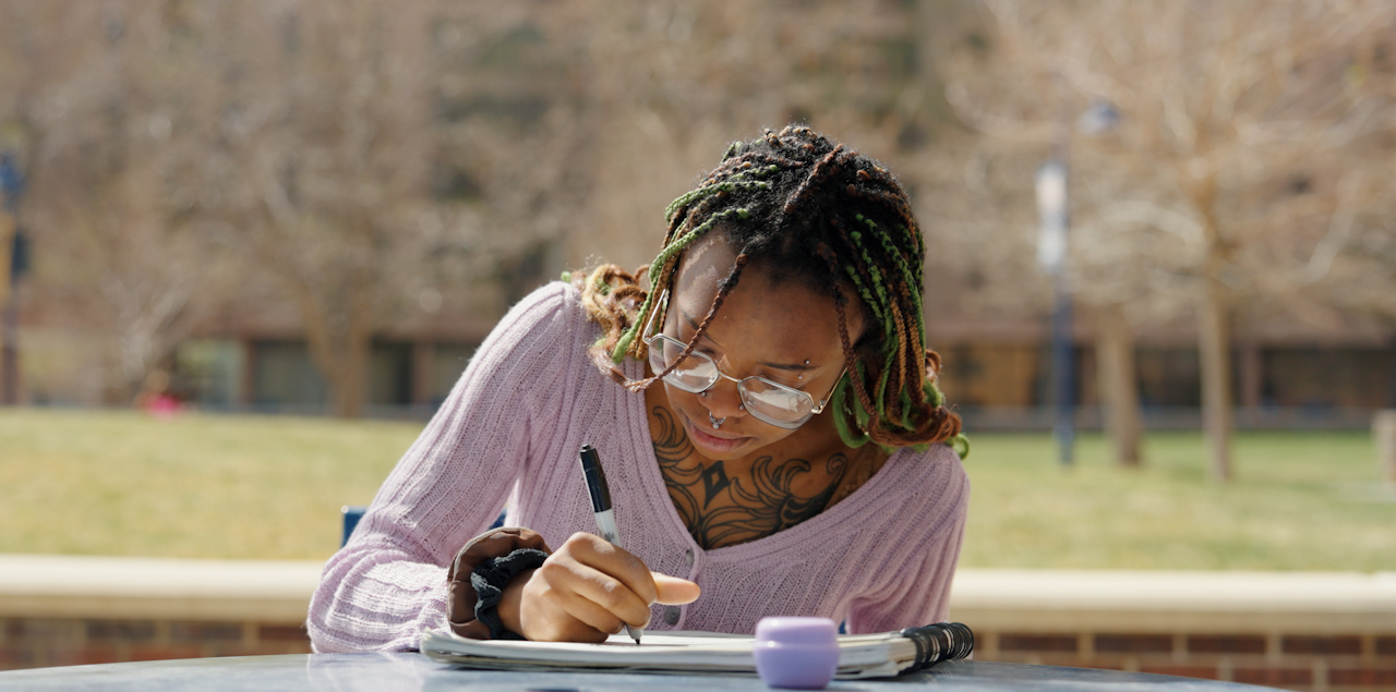 Ann-Adele Blassingame sitting on a table outside drawing.