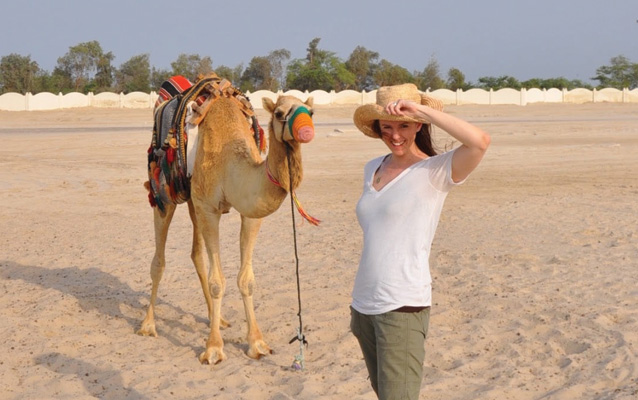 Karen Barton posing in front of a camel in the sand.