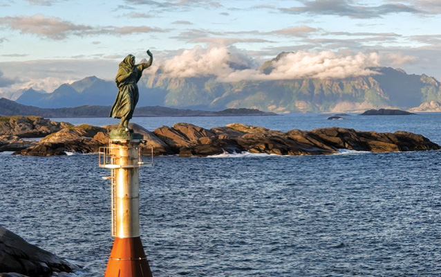 A rocky ocean inlet next to a statue of a person standing atop a metal pole.