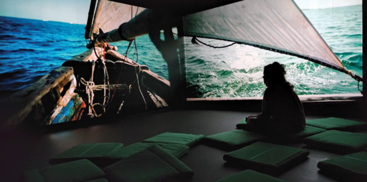 Karen Barton sitting in a dark room surrounded by screens showing the ocean.