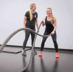 Student personal trainer encouraging student participant who is using battle ropes.