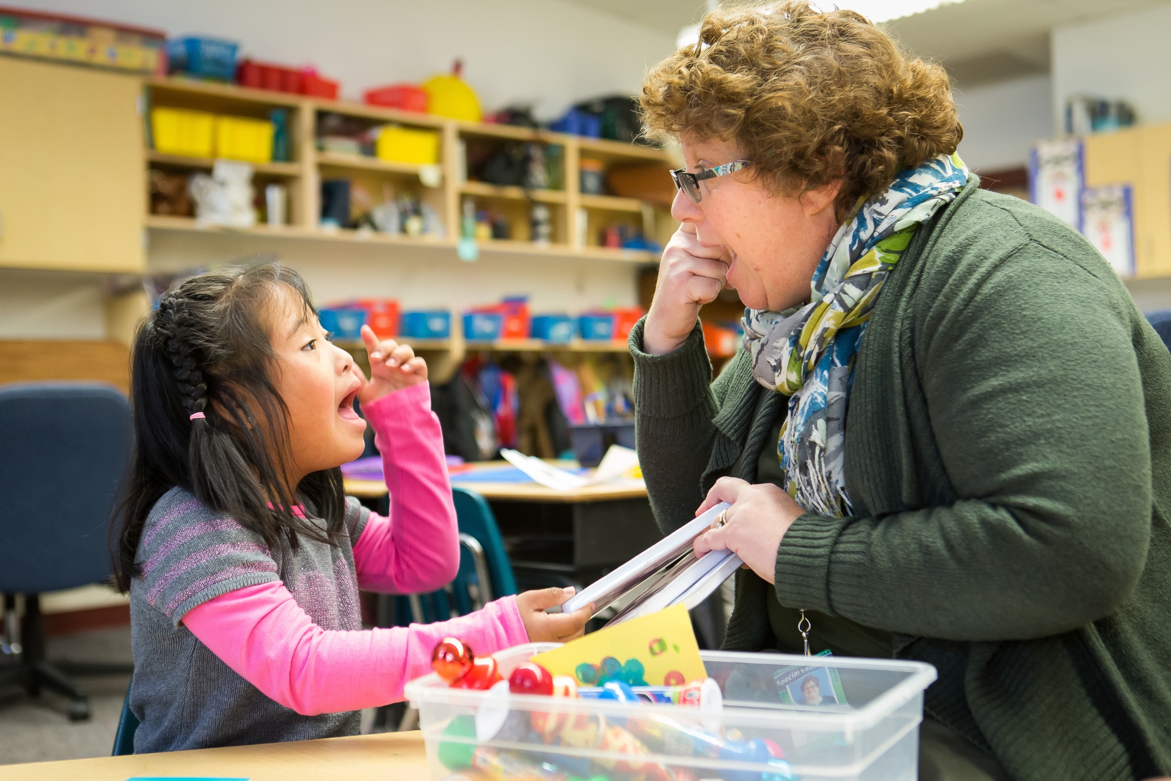 A lady is pointing at her eye to a young girl