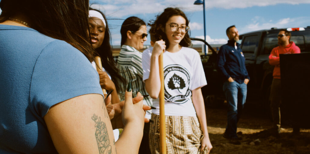A student smiling at the camera outside holding a shovel
