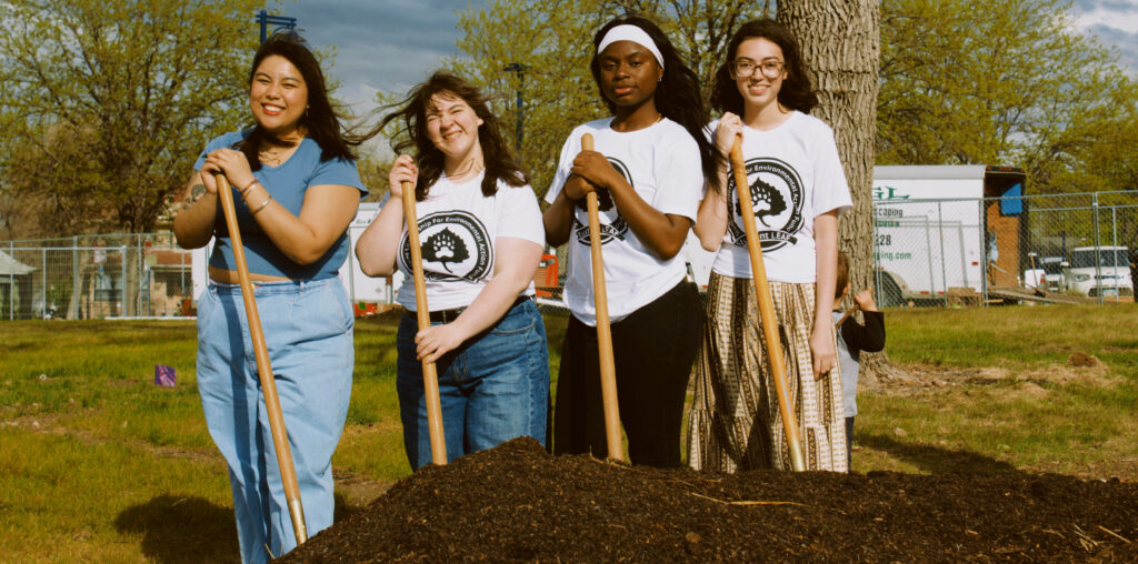 Student LEAF members smiling in front of compost pile holding shovels