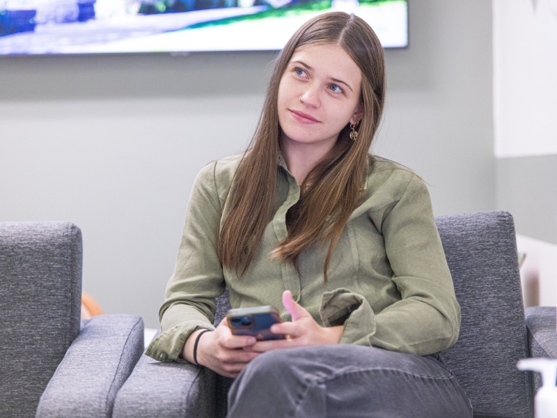 A female student is waiting in the counseling room. She is sitting down and shown smiling off in the distance.