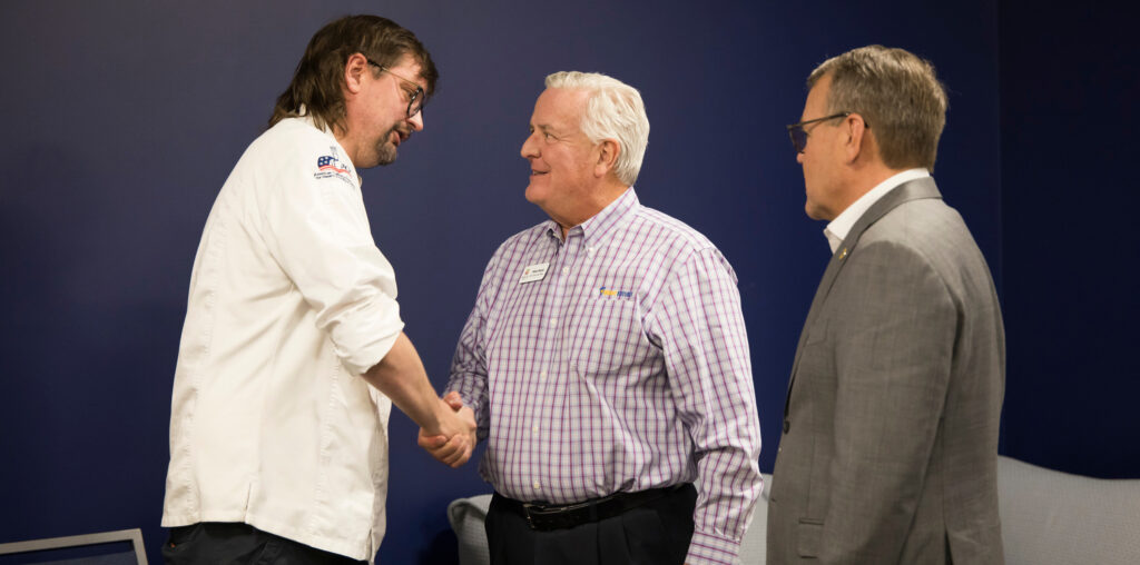 Two men shaking hands with a third standing nearby