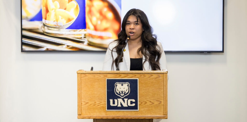Taylor Schiestel talking into a microphone behind a podium