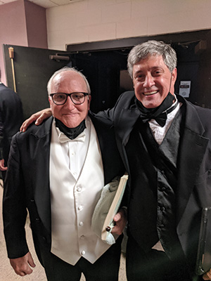 Two gentlemen with their arms wrapped around each other smiling