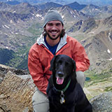 A picture of David Lerach on a mountain posing with his black lab