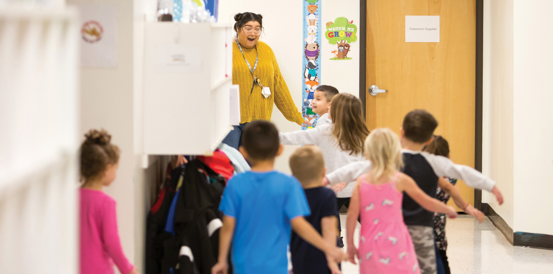 A teacher welcoming her young students into a classroom