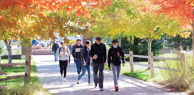 Students walking on campus under trees sporting fall leaves