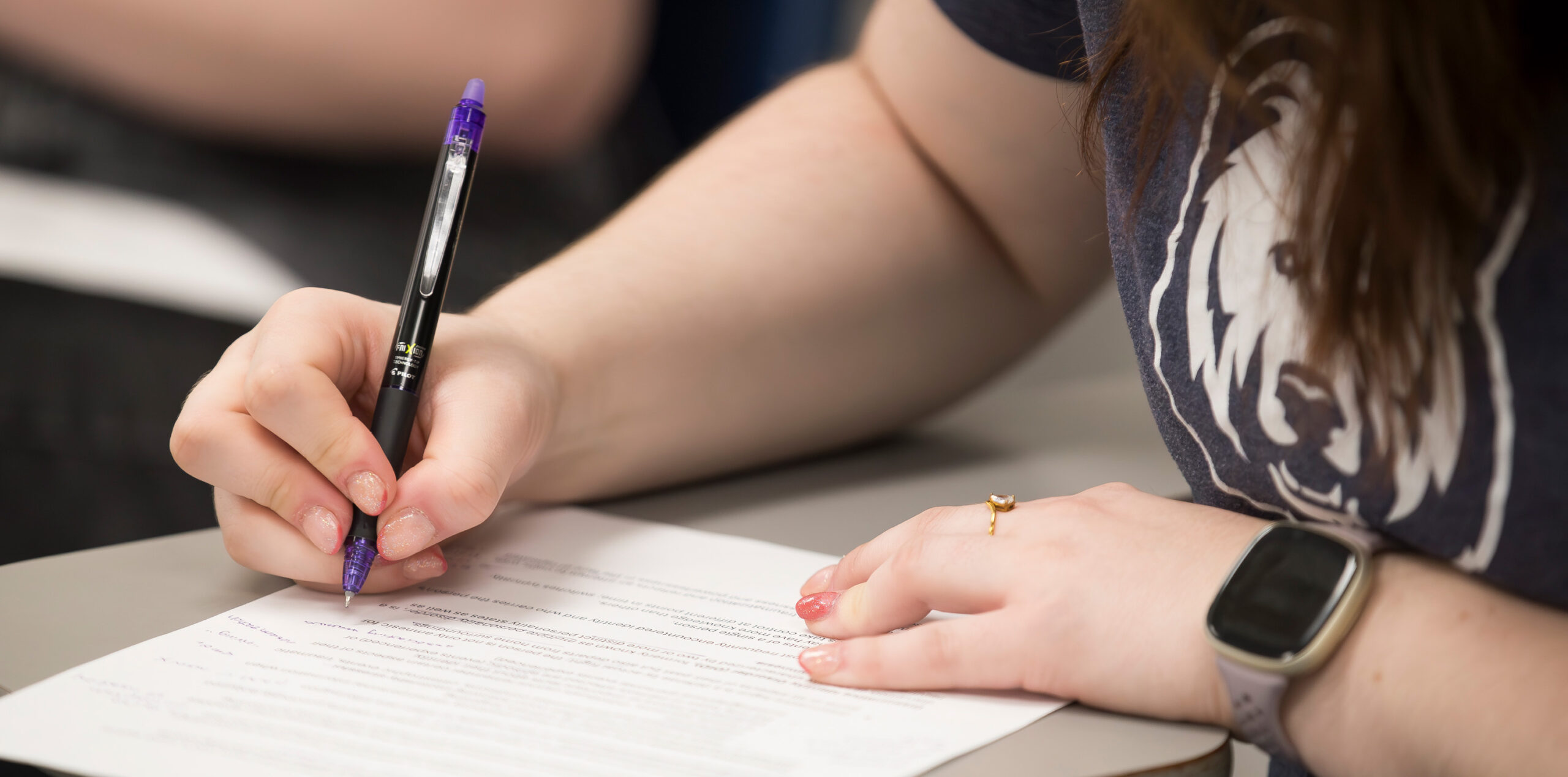 A student writing on a piece of paper with a purple pen