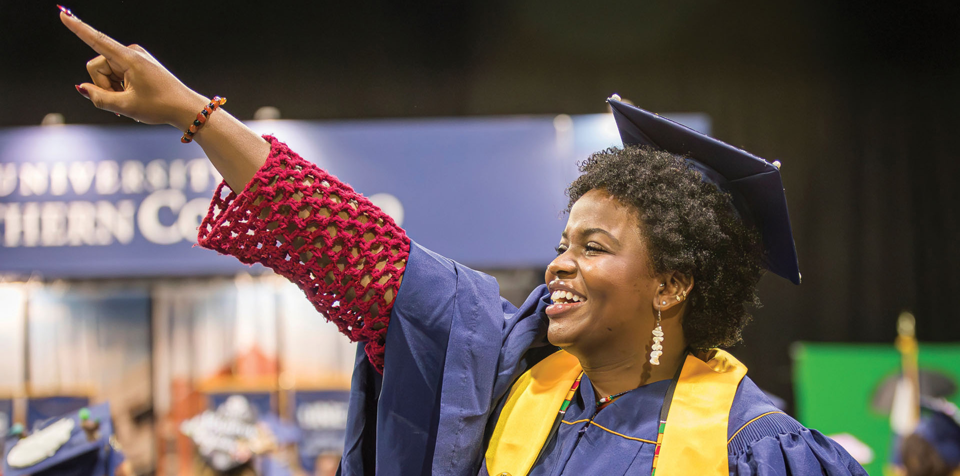 A graduate pointing up at the stands at the ceremony