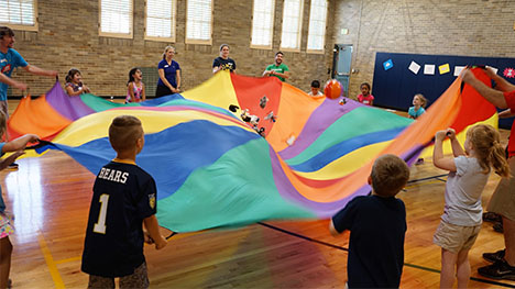 Kids playing a game that involves using a parachute to bounce soft items