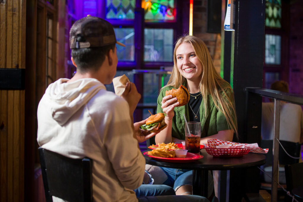 Two people sitting down and eating burgers at a restaurant