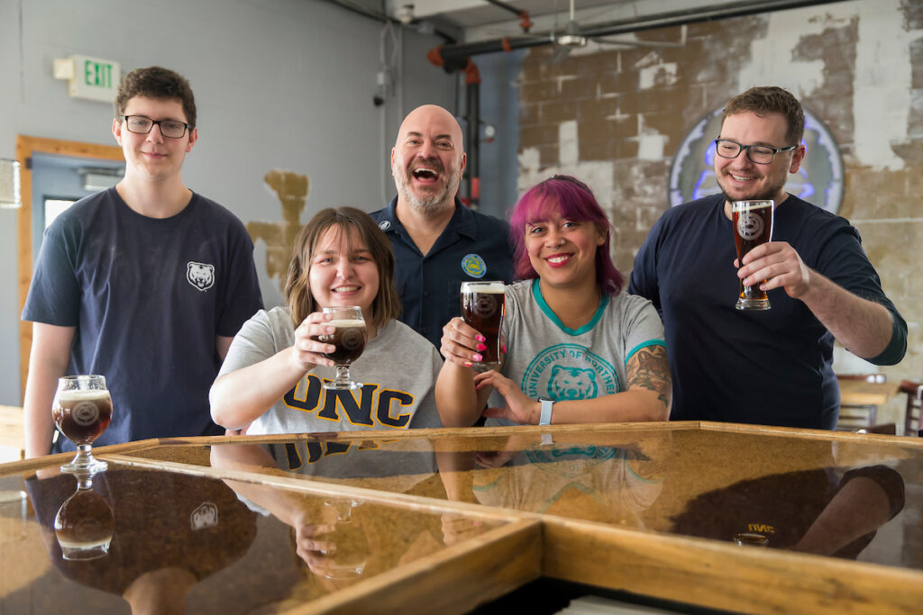 A group of people holding up beers and smiling at a bar